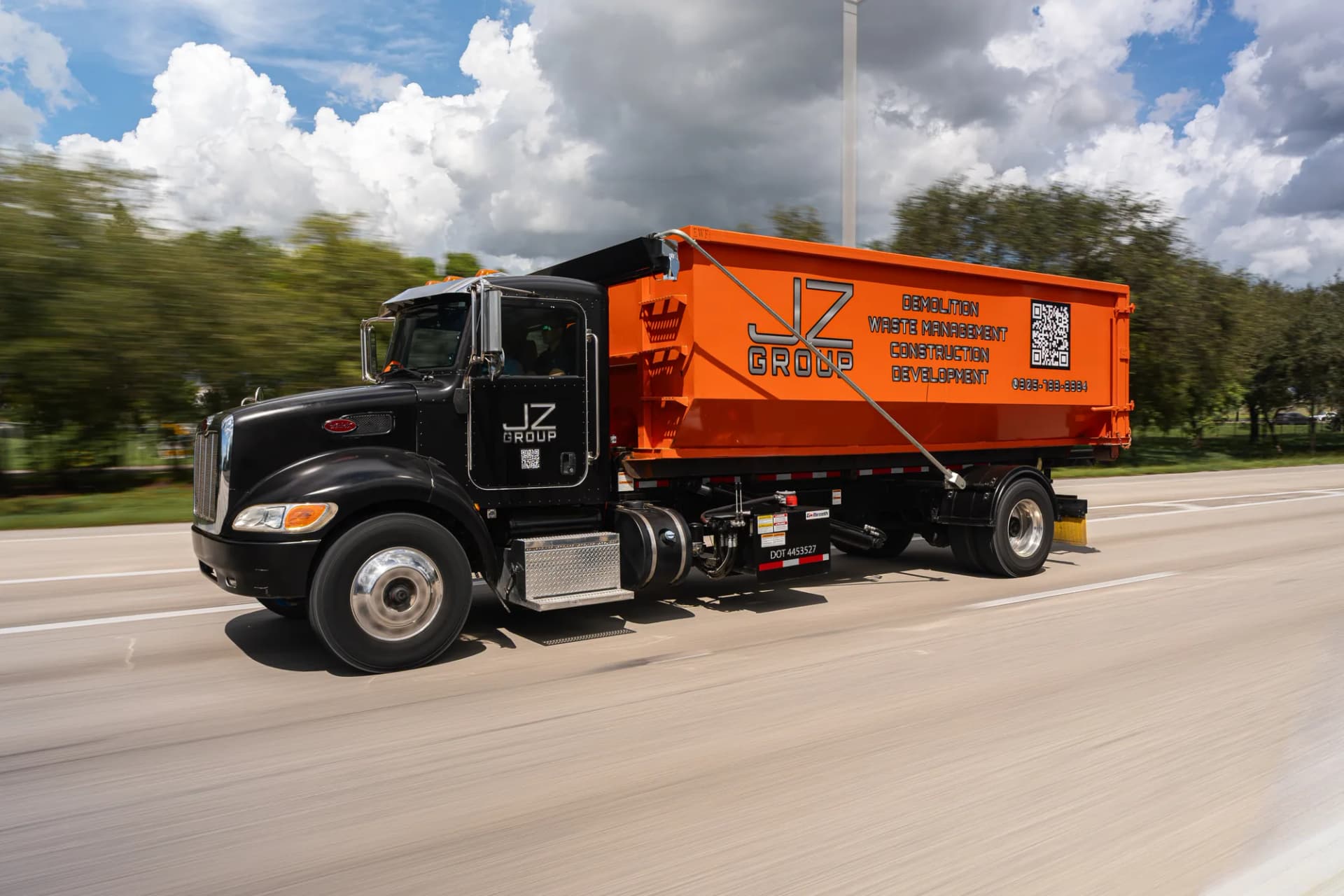 JZ Waste Management truck carrying an orange roll-off container