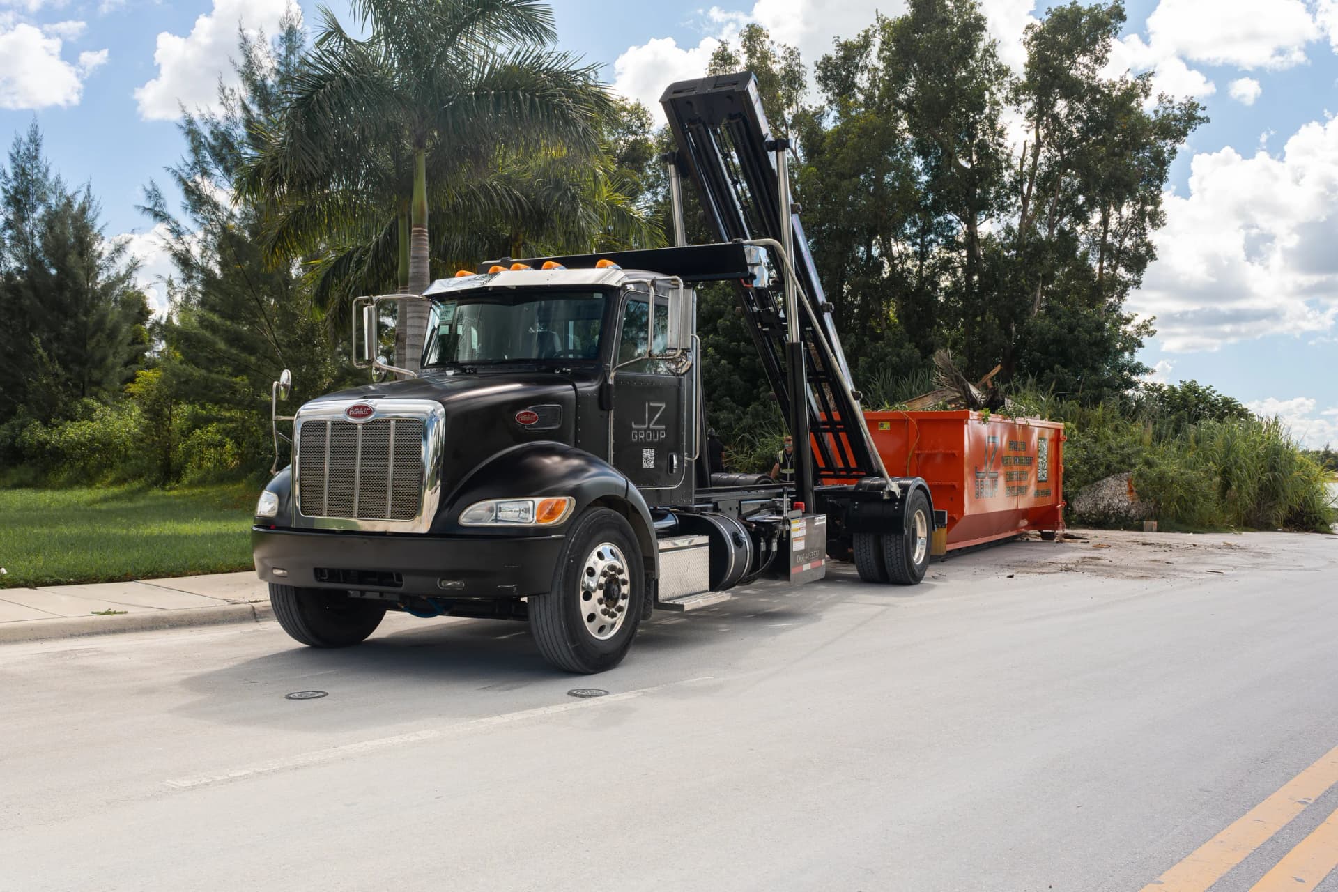Black JZ hauling truck with a raised roll-off mechanism and an orange container